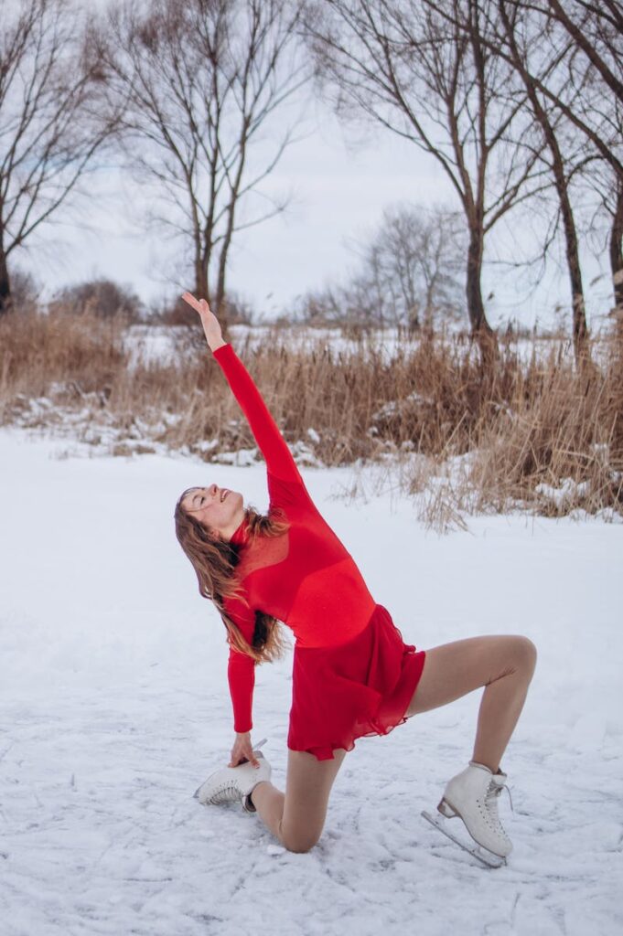 A woman in a red dress performs a graceful pose while ice skating on a snowy day.