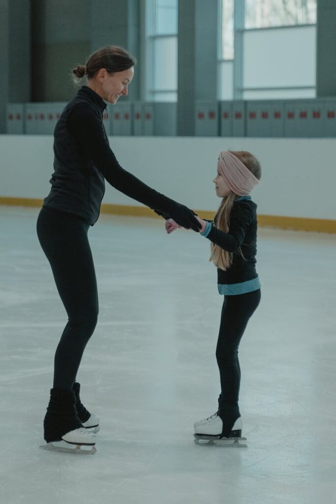 A mother teaches her daughter the basics of ice skating in an indoor rink.