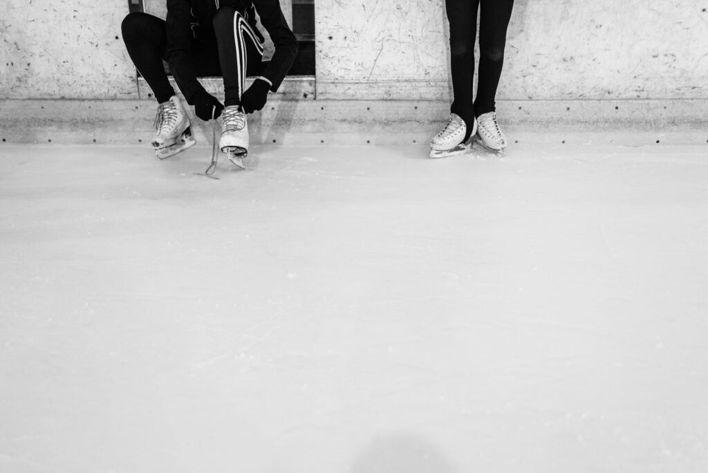 Monochrome image of individuals preparing for ice skating on a rink.